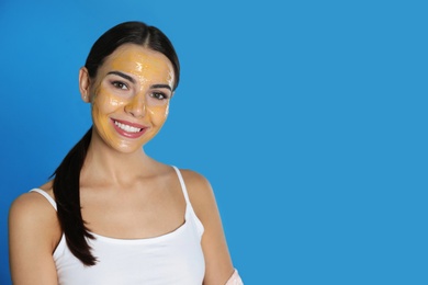 Young woman with cleansing mask on her face against color background, space for text. Skin care