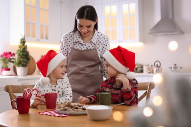 Photo of Mother and her cute little children with Christmas cookies in kitchen