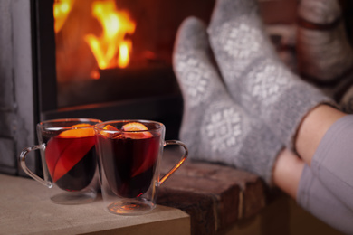 Tasty mulled wine in glass cups near fireplace indoors