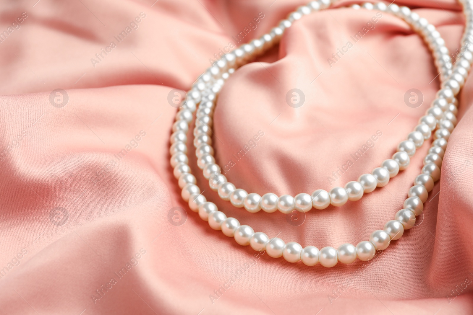 Photo of Elegant necklace with pearls on pink silk, closeup