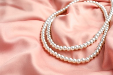 Photo of Elegant necklace with pearls on pink silk, closeup