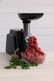 Photo of Electric meat grinder with beef mince, garlic and parsley on white wooden table