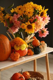 Photo of Autumn composition with beautiful flowers and pumpkins on console table near dark grey wall