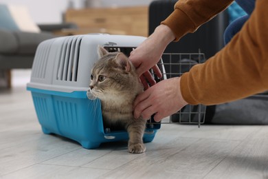 Photo of Travel with pet. Man near carrier with cute cat at home, closeup