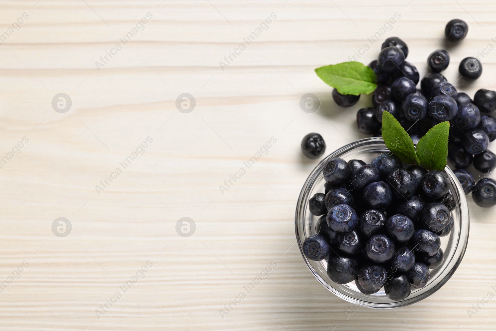 Photo of Ripe bilberries and leaves on white wooden table, flat lay. Space for text