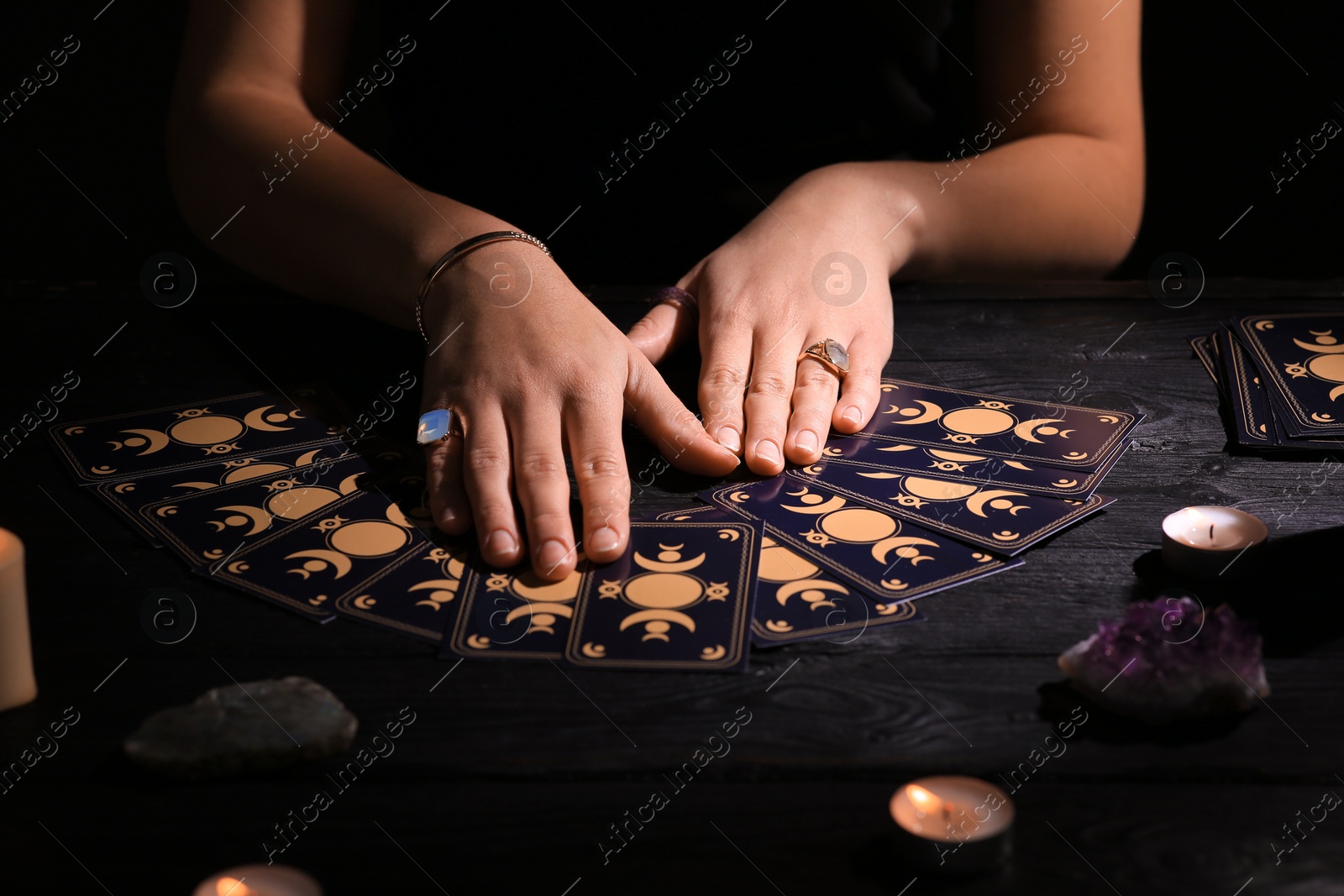 Photo of Soothsayer predicting future with tarot cards at table in darkness, closeup