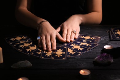 Photo of Soothsayer predicting future with tarot cards at table in darkness, closeup