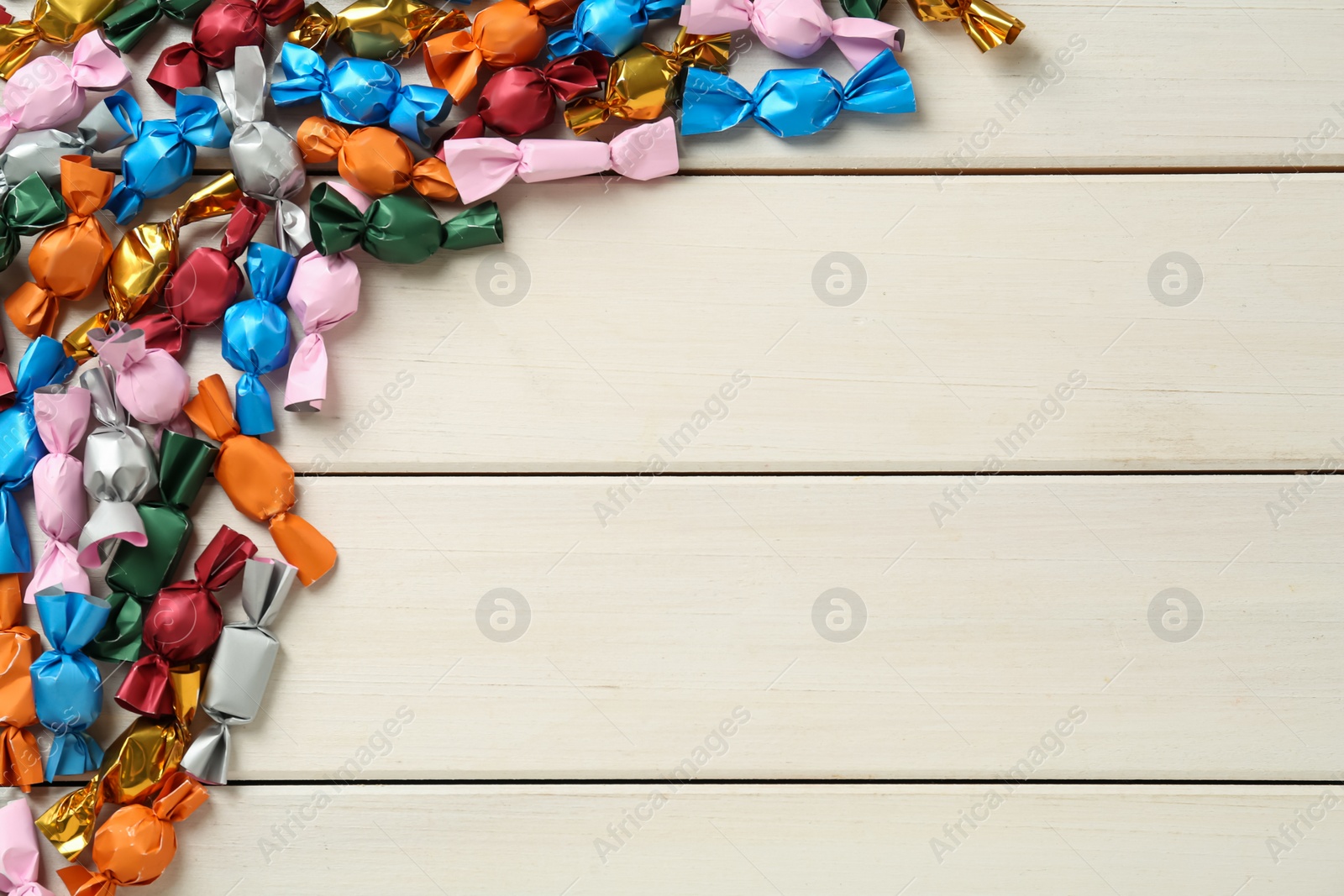 Photo of Candies in colorful wrappers on beige wooden table, flat lay. Space for text