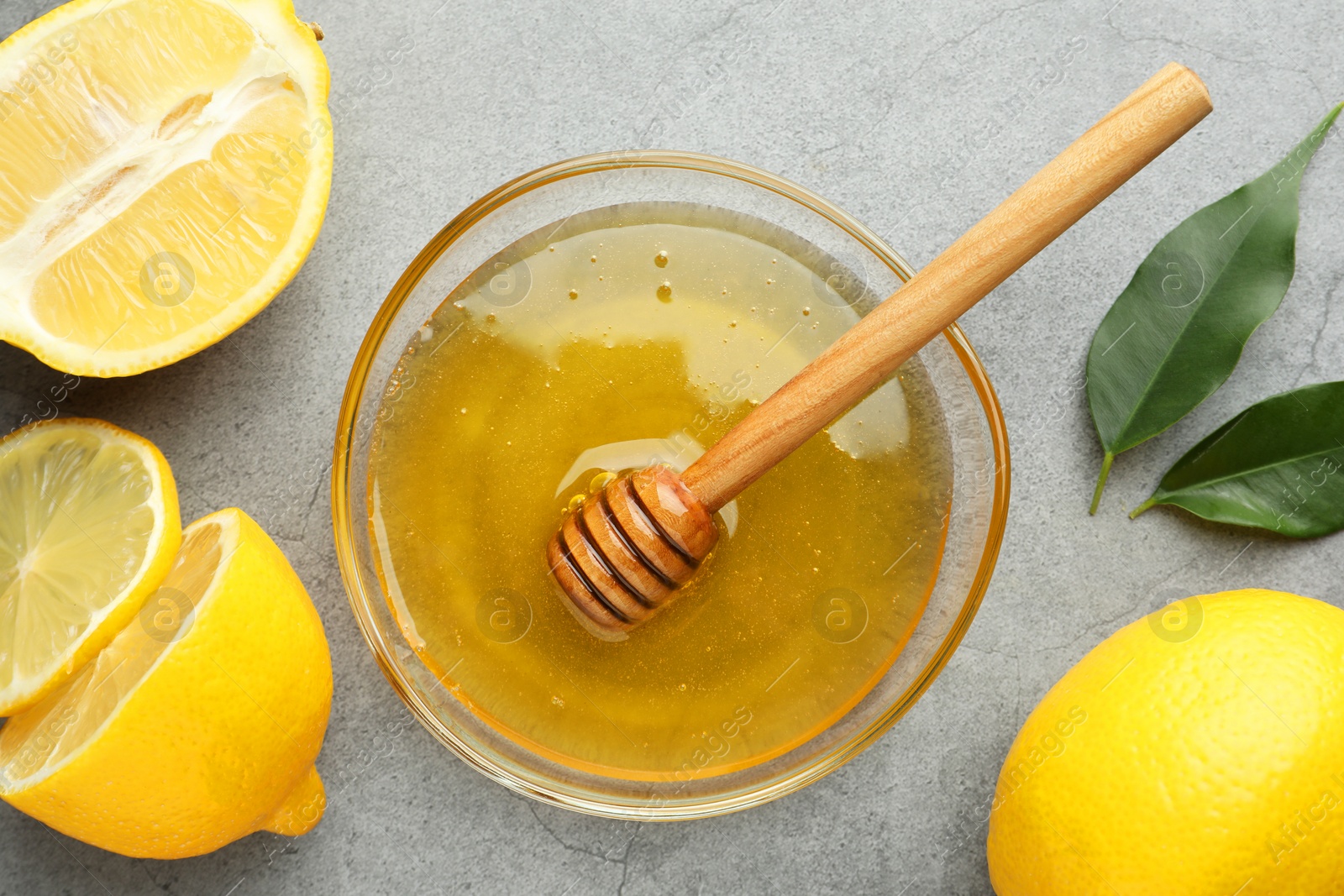 Photo of Sweet honey and fresh lemons on grey table, flat lay