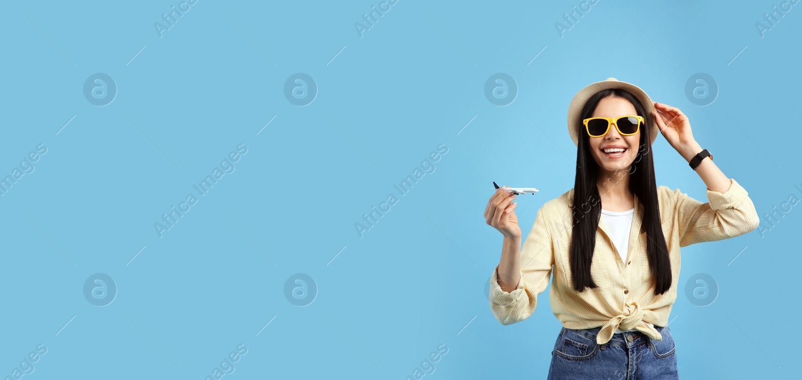 Photo of Happy female tourist with toy plane on light blue background. Space for text