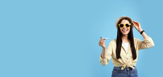 Photo of Happy female tourist with toy plane on light blue background. Space for text