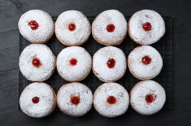 Many delicious donuts with jelly and powdered sugar on black table, top view