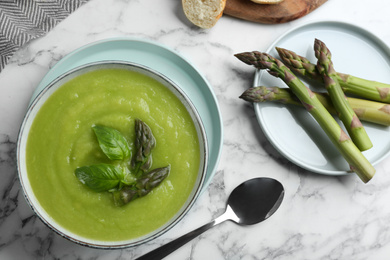 Photo of Delicious asparagus soup in bowl on white marble table, flat lay