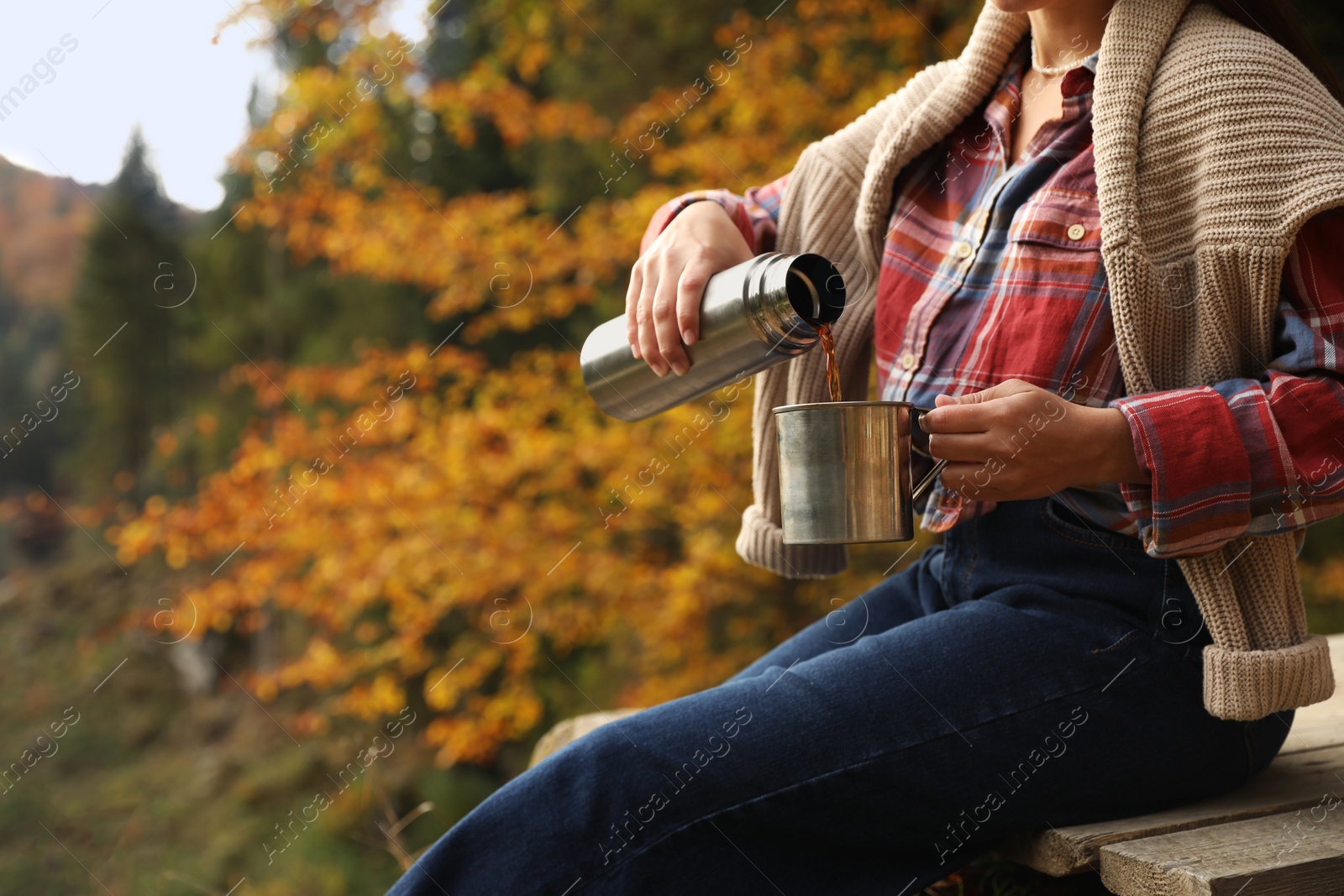 Photo of Woman pouring hot drink from thermos into metallic mug outdoors, closeup. Space for text