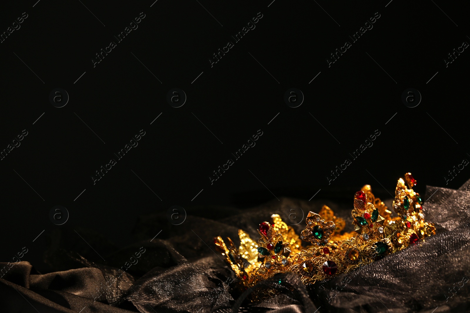 Photo of Beautiful golden crown with gems on dark cloth. Space for text