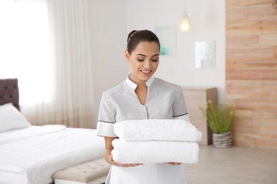 Photo of Young chambermaid with clean towels in bedroom