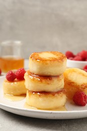 Delicious cottage cheese pancakes with raspberries and honey on light grey table, closeup