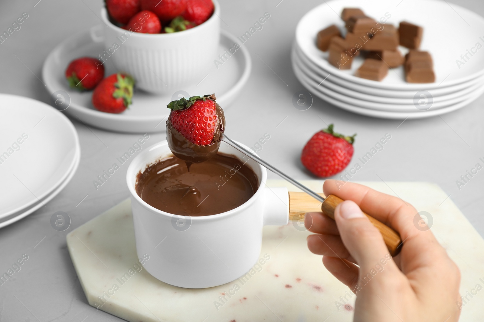 Photo of Woman dipping strawberry into fondue pot with chocolate at grey table, closeup