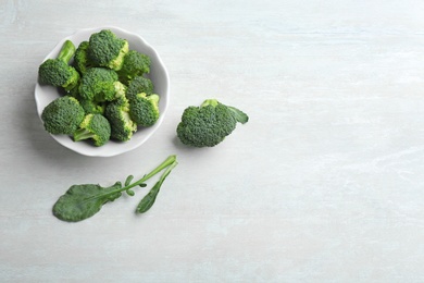 Photo of Bowl of fresh broccoli and leaves on light grey table, flat lay with space for text