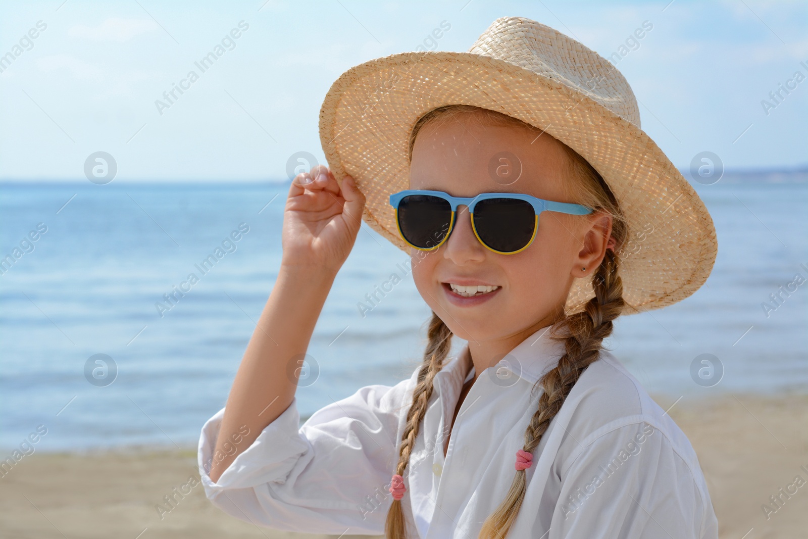 Photo of Little girl wearing sunglasses and hat at beach on sunny day