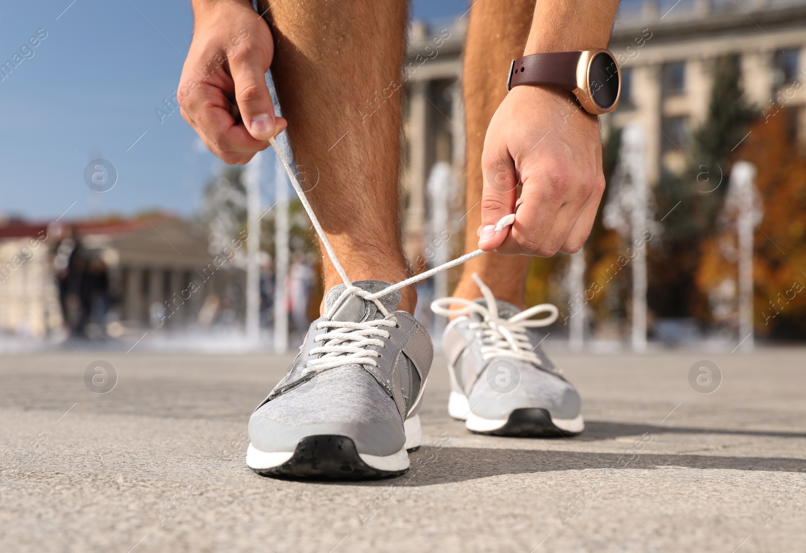 Image of Sporty man tying shoelaces outdoors on sunny morning, closeup