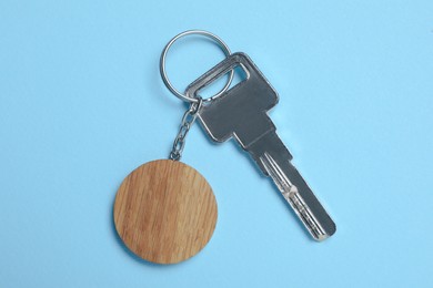 Photo of Key with wooden keychain in shape of smiley face on light blue background, top view