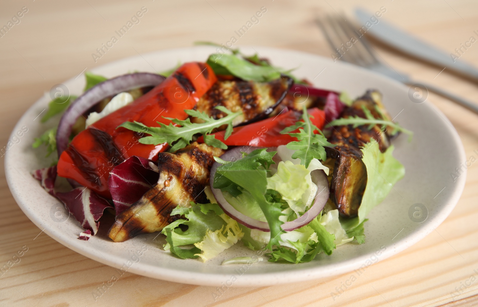 Photo of Delicious salad with roasted eggplant and arugula served on wooden table, closeup