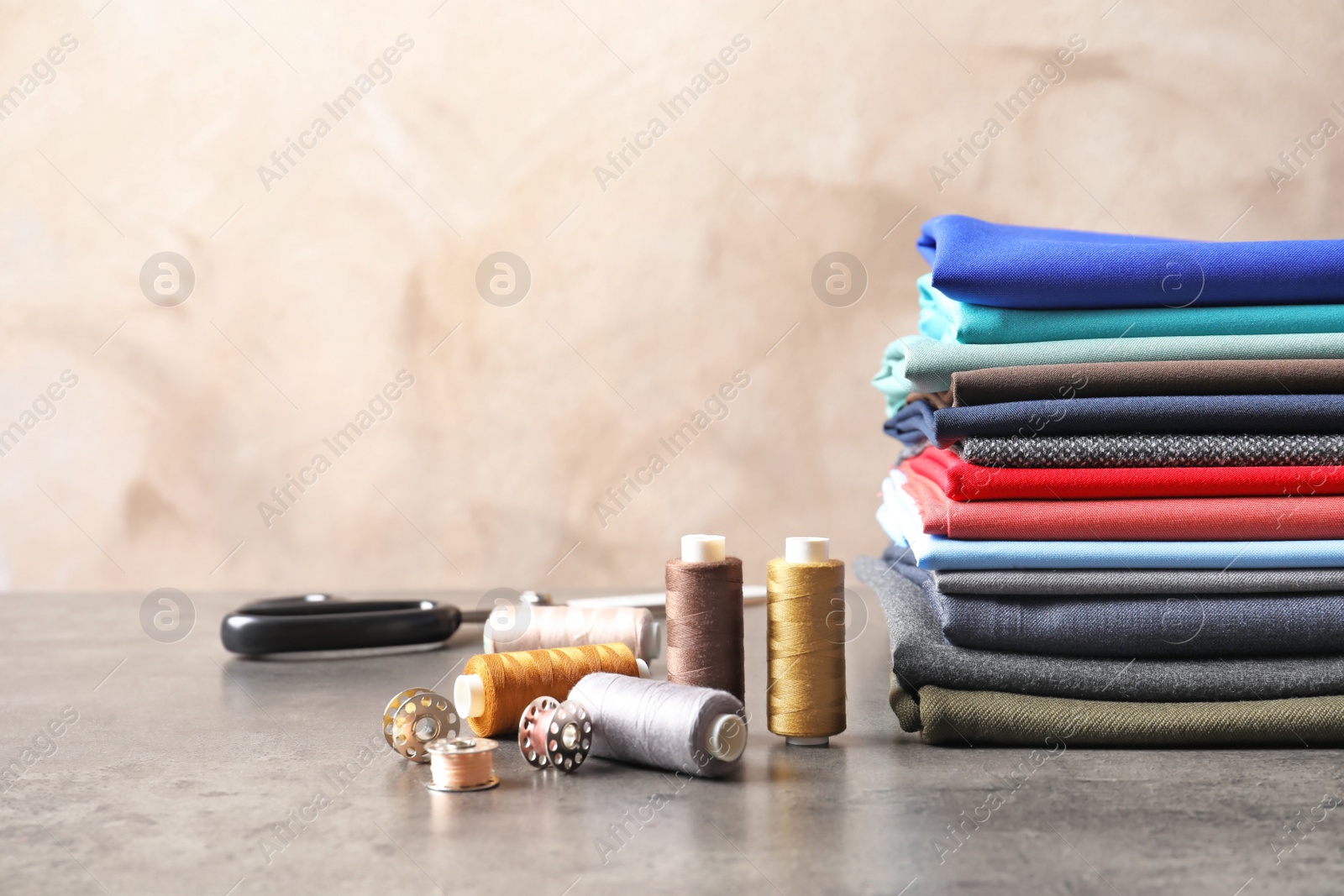 Photo of Bobbins with threads and stack of colorful fabrics on table. Tailoring accessories