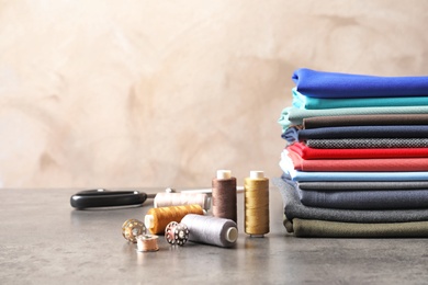 Bobbins with threads and stack of colorful fabrics on table. Tailoring accessories