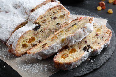 Photo of Traditional Christmas Stollen with icing sugar on black table, closeup