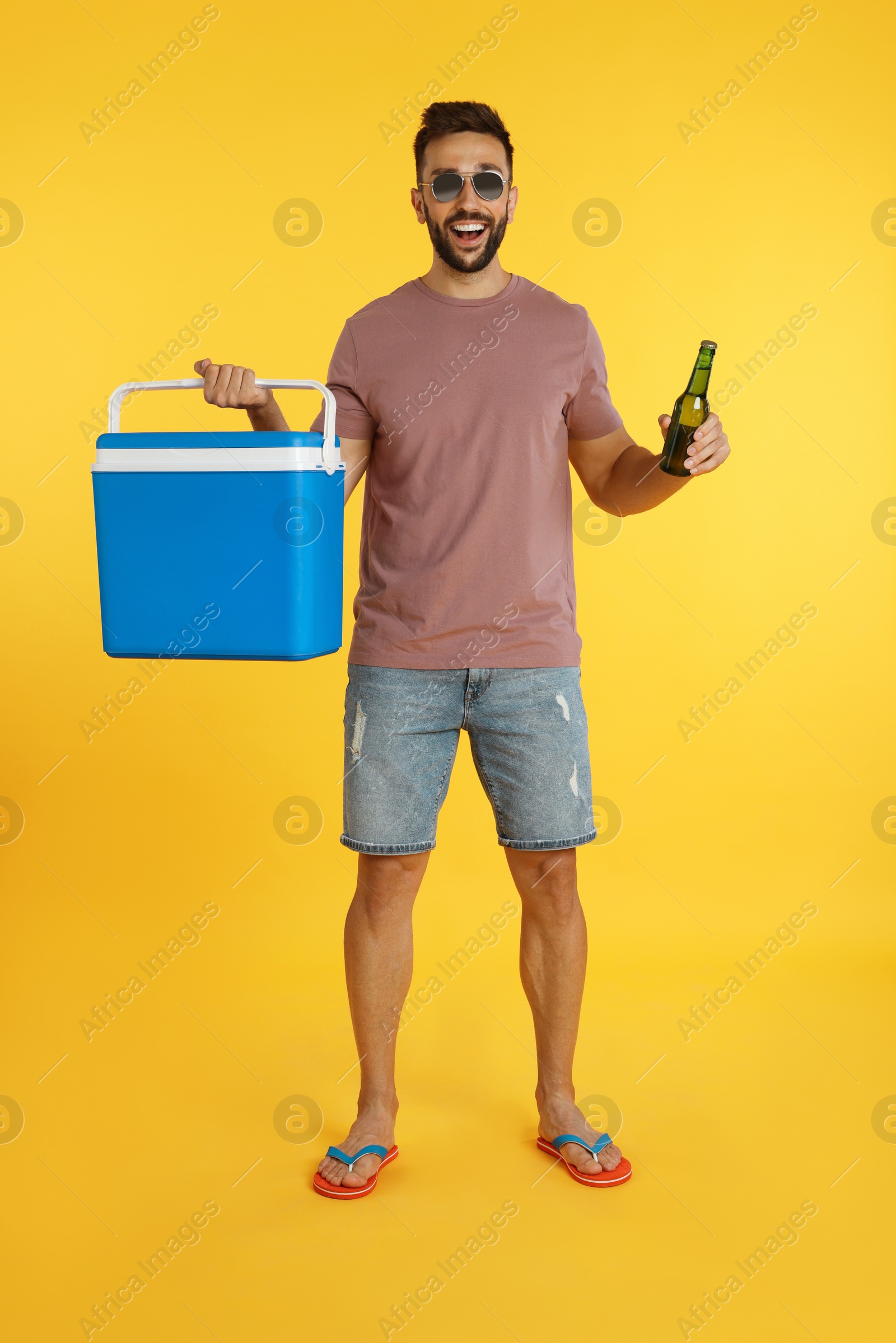 Photo of Happy man with cool box and bottle of beer on yellow background