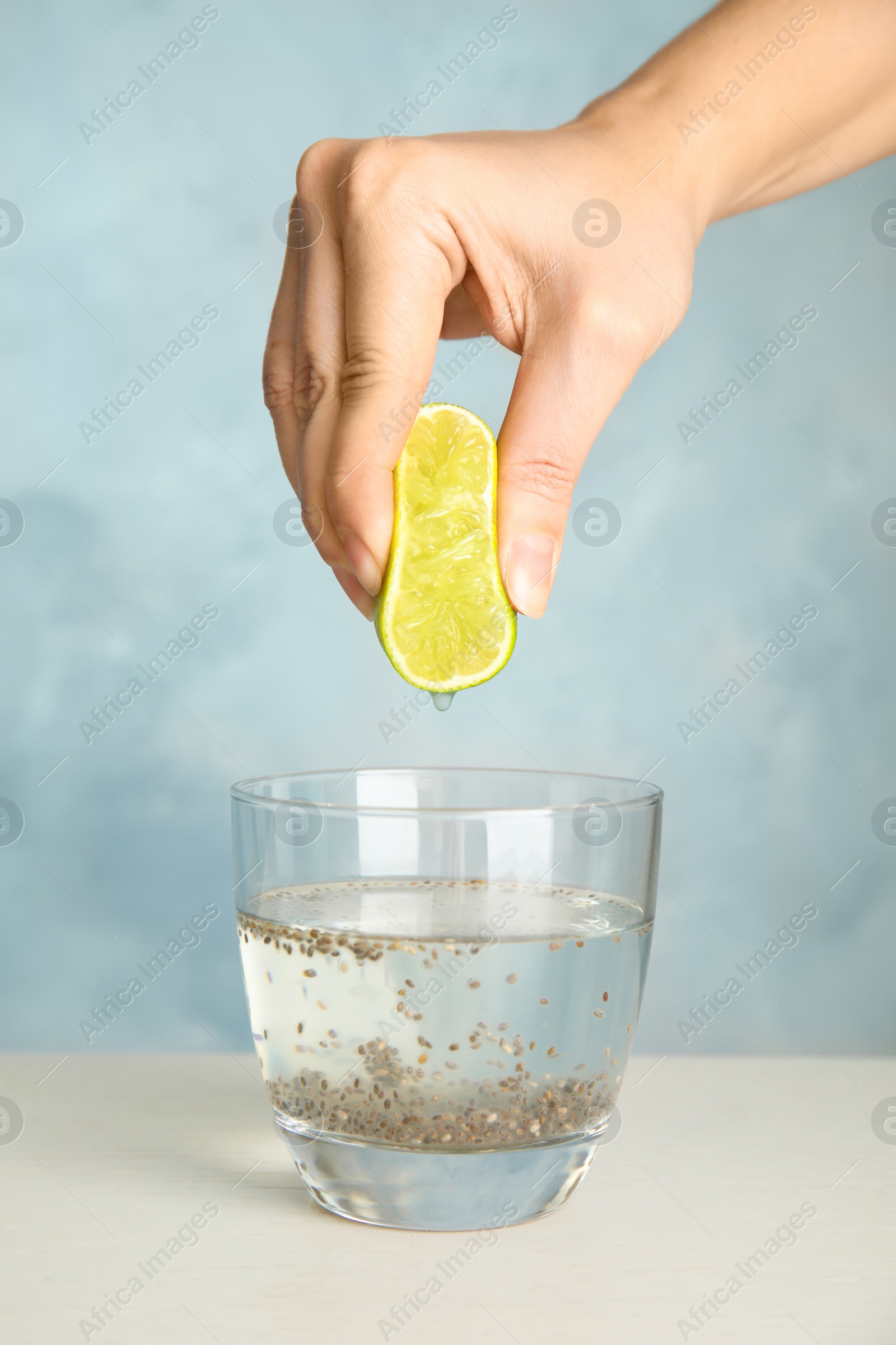 Photo of Young woman squeezing lime into glass of water with chia seeds on table, closeup