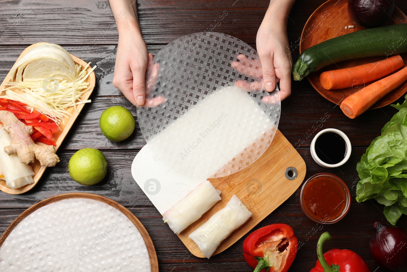 Photo of Making delicious spring rolls. Woman with fresh rice paper at wooden table, flat lay