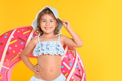 Cute little child in beachwear with bright inflatable ring on yellow background