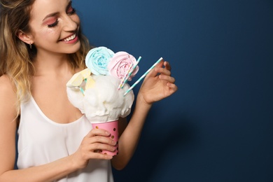 Young woman holding cotton candy dessert on blue background. Space for text