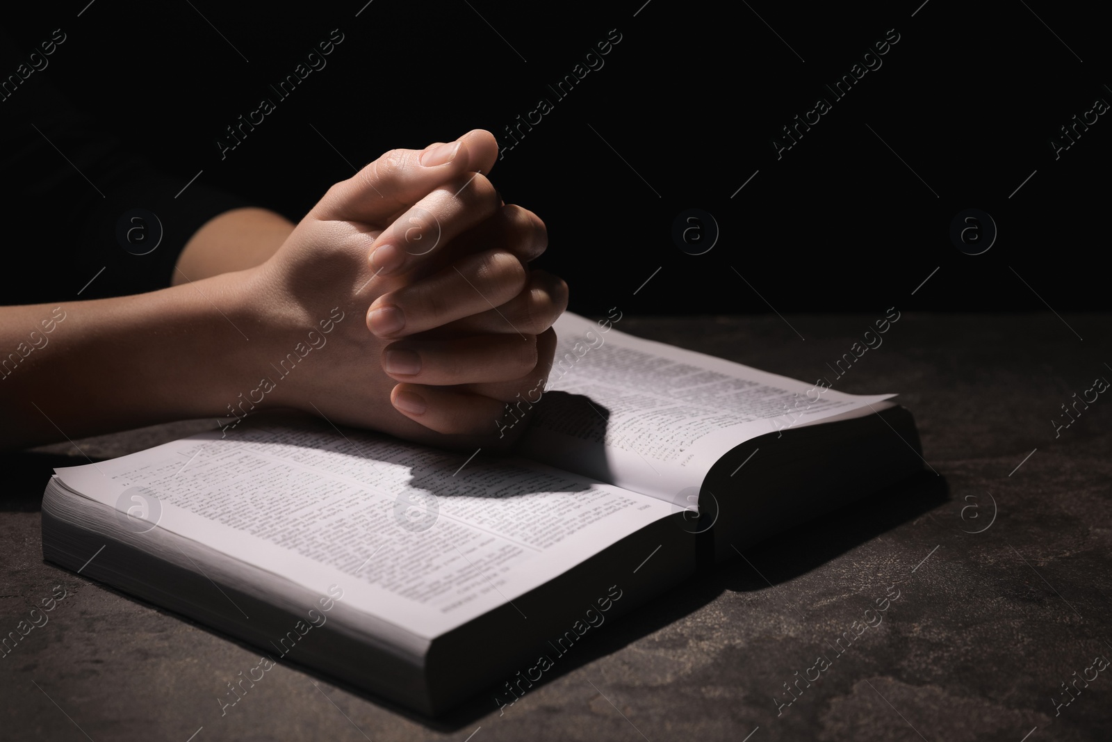 Photo of Religion. Christian woman praying over Bible at table against black background, closeup. Space for text