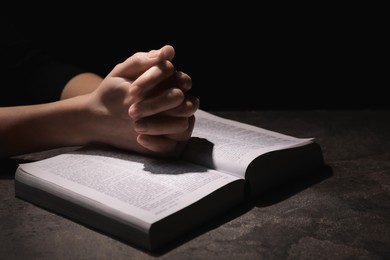 Religion. Christian woman praying over Bible at table against black background, closeup. Space for text