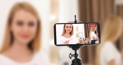 Image of Woman applying makeup in room, selective focus on smartphone display