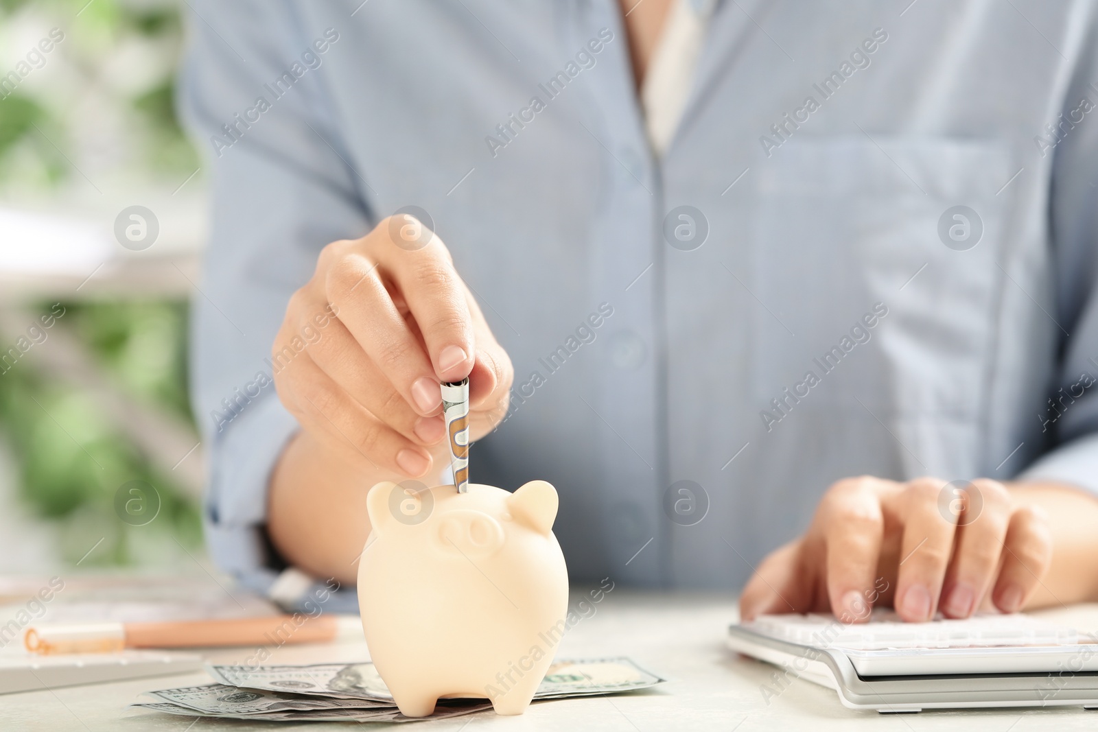 Photo of Woman putting money into piggy bank at table, closeup