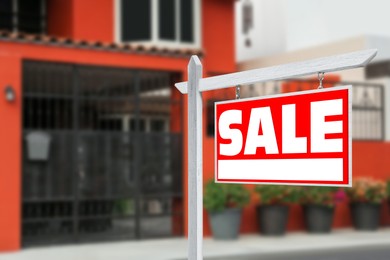 Image of Sale sign near beautiful house outdoors. Red signboard with word