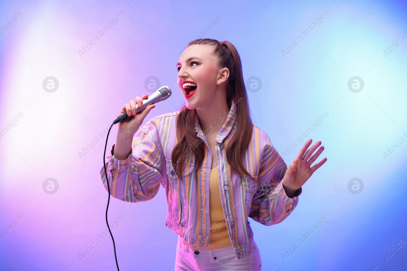 Photo of Emotional woman with microphone singing in color lights