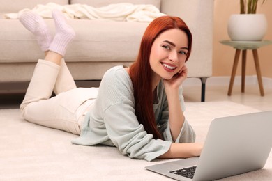Photo of Happy woman with red dyed hair lying on floor near laptop at home