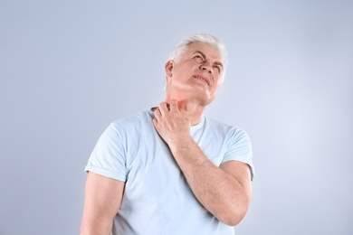 Senior man scratching neck on grey background. Allergy symptom