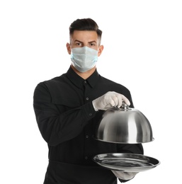 Photo of Waiter in medical face mask holding tray with lid on white background