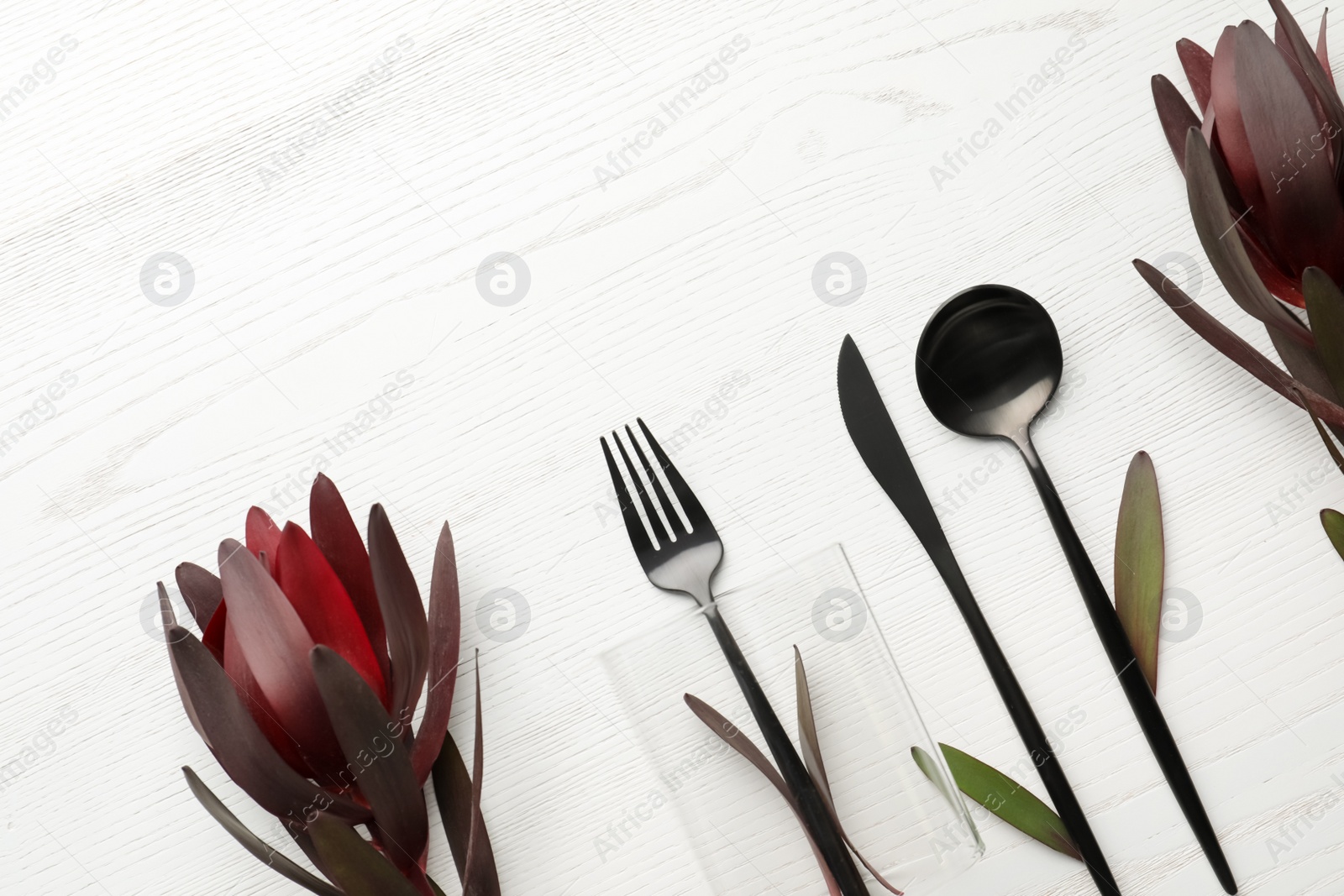 Photo of Cutlery and floral decor on white wooden background, space for text. Table setting elements