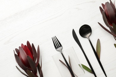 Cutlery and floral decor on white wooden background, space for text. Table setting elements