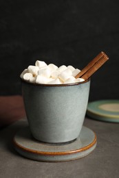 Mug of delicious drink with marshmallows and stylish cup coaster on grey table