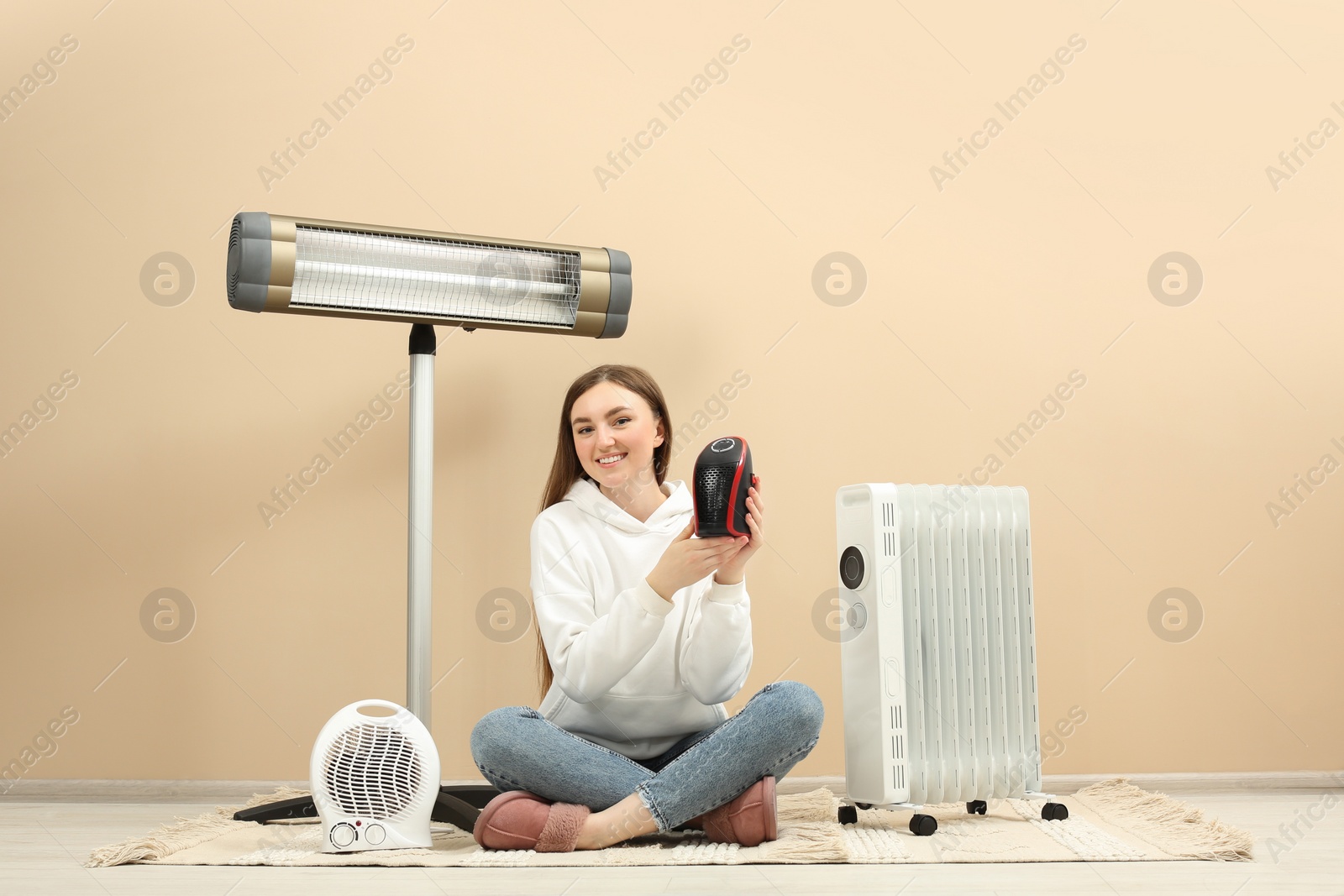 Photo of Young woman with different modern electric heaters near beige wall indoors