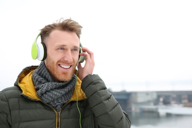 Photo of Young man listening to music with headphones outdoors. Space for text