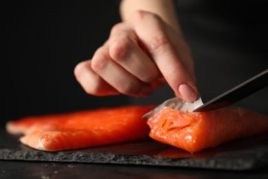 Photo of Chef removing scales from salmon for sushi at dark table, closeup